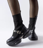 Black sock-like knit ankle boots with chunky platform, silver buckles, and sleek design showcased in stylish polka dot tights.