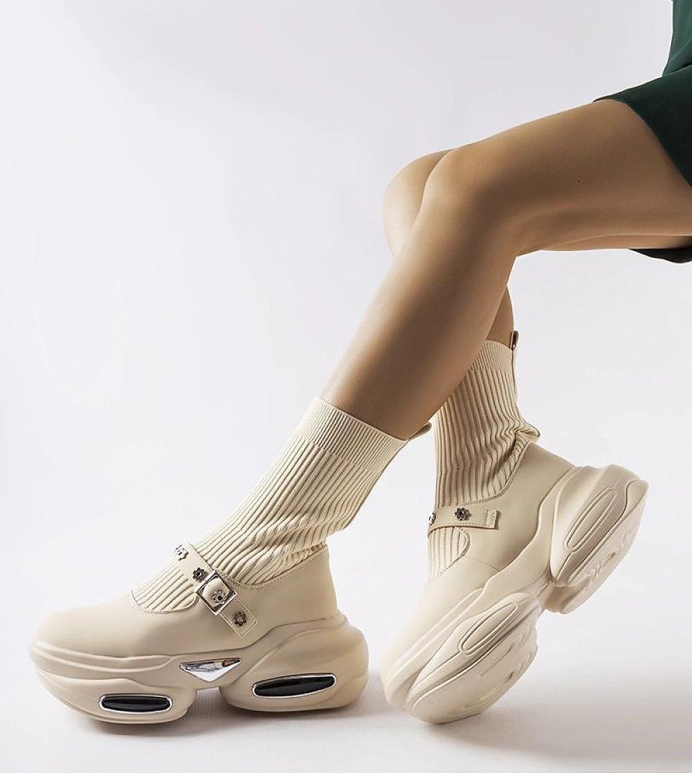Woman wearing Elvessa stretch knit ankle boots with sculpted heels and sock-like beige upper, pairing with beige socks and a green dress.