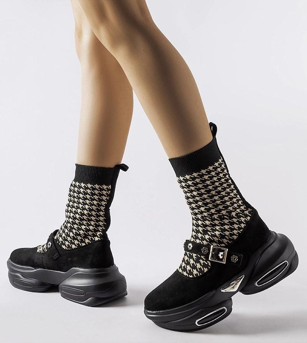 Person wearing black and white houndstooth knit socks with black platform sneakers and shiny buckles.