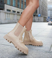 Woman wearing beige high-heel zip boots with treaded sole on urban street, showcasing stylish and comfortable footwear.