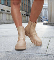 Stylish deep beige high-heel zip boots with rounded toe and treaded sole, perfect for pairing with casual outfits. Urban background view.