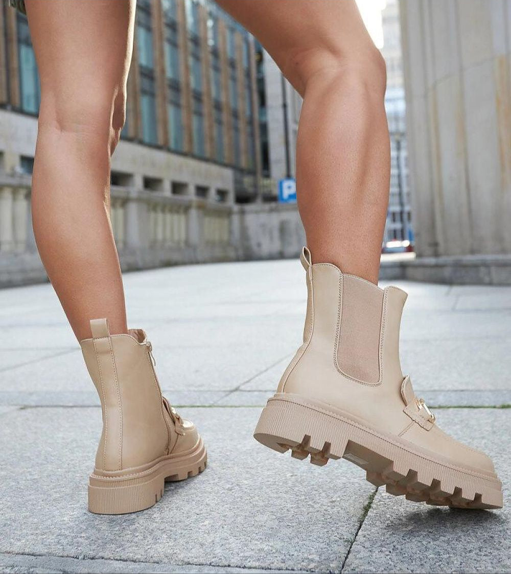 Woman wearing beige high-heel zip boots with a treaded sole, showcasing urban style and comfort.