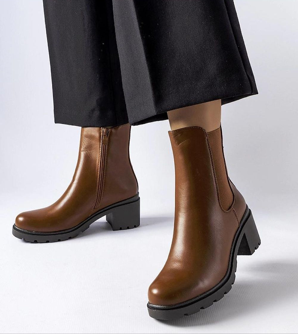 Model wearing Carserra ankle-heel boots in brown eco leather with sleek stiletto heel and zipper closure for elegant style.