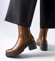 Brown Carserra ankle-heel boots in eco leather with stiletto heel, paired with black pants for elegant everyday wear.