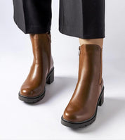 Brown ankle-high Carserra boots with stiletto heels and eco leather finish, paired with black pants for a chic look.