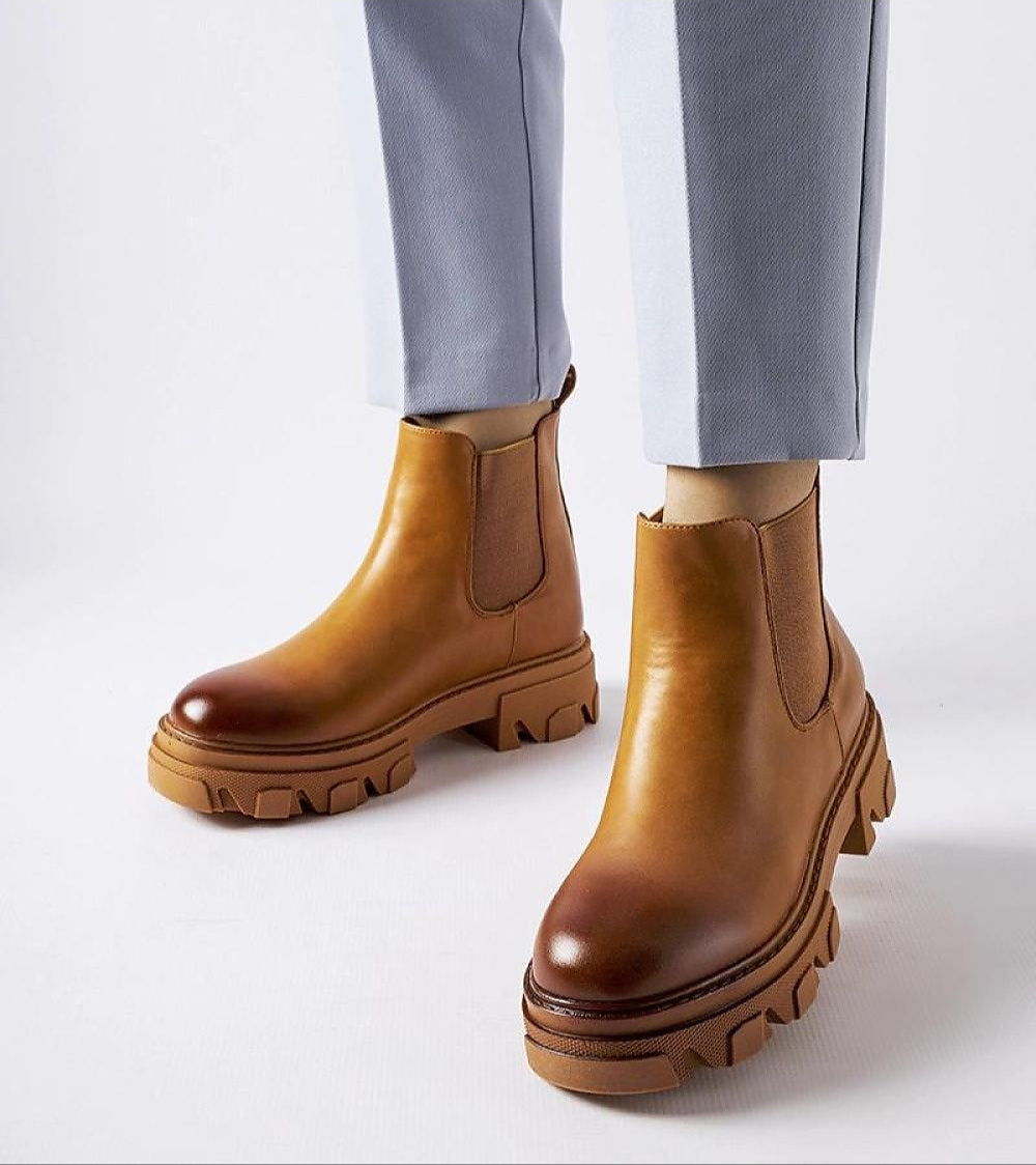 Person wearing Sorava ankle slip-on boots in brown with rugged sole and eco leather finish, paired with light-colored trousers.