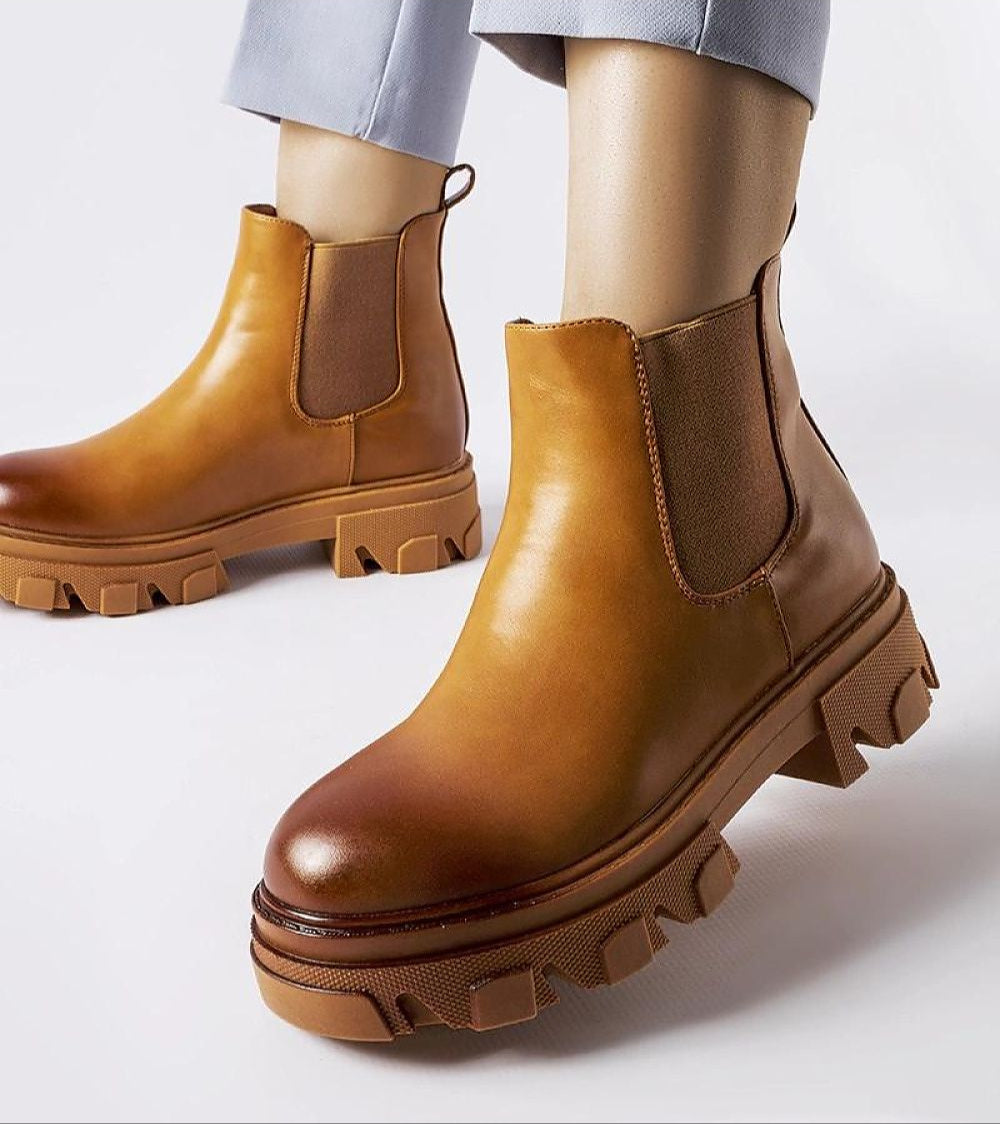 Person wearing brown Sorava Ankle Slip-On Boots with rounded toe and thick sole for stylish and comfortable everyday wear.