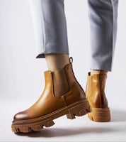 Person wearing Sorava Ankle Slip-On Boots with brown eco leather, rounded toe, and 5 cm heel, showcasing sleek and stylish footwear.