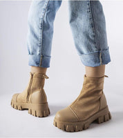 Person wearing tan suede platform boots with rugged soles and jeans, showcasing stylish fall footwear.