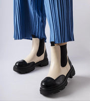 Albany Two-Tone Rubber Platform Boots in black and beige, worn with blue pleated pants, showcasing a minimalist and weather-resistant design.