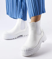 White slip-on boots with rubber insets and platform heel worn with blue pleated pants for a stylish urban look.