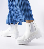 Woman wearing stylish white slip-on boots with blue pleated skirt.
