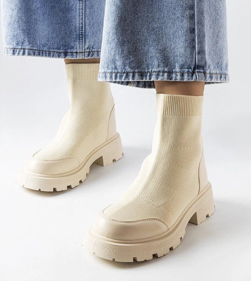 Beige stretch-knit sock boots with high upper and medium heel, styled with denim jeans for a chic, elegant look.