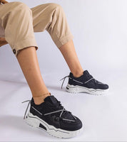 Person wearing Nimvara shimmer detail black sneakers with a white sole, showcasing modern design and eco leather finish.