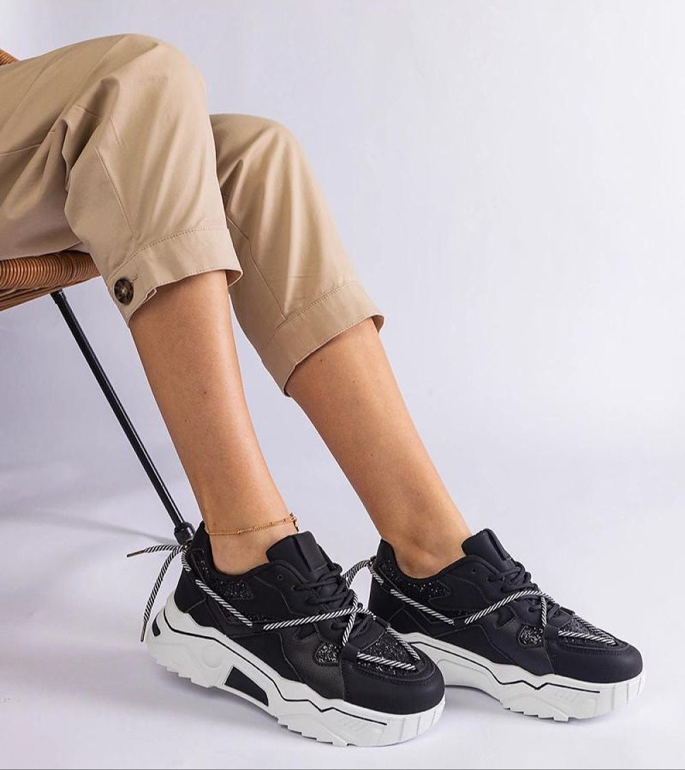 Nimvara Shimmer Detail Black Sneakers with eco leather and brocade accents, featuring a white rubber sole, worn with beige pants.