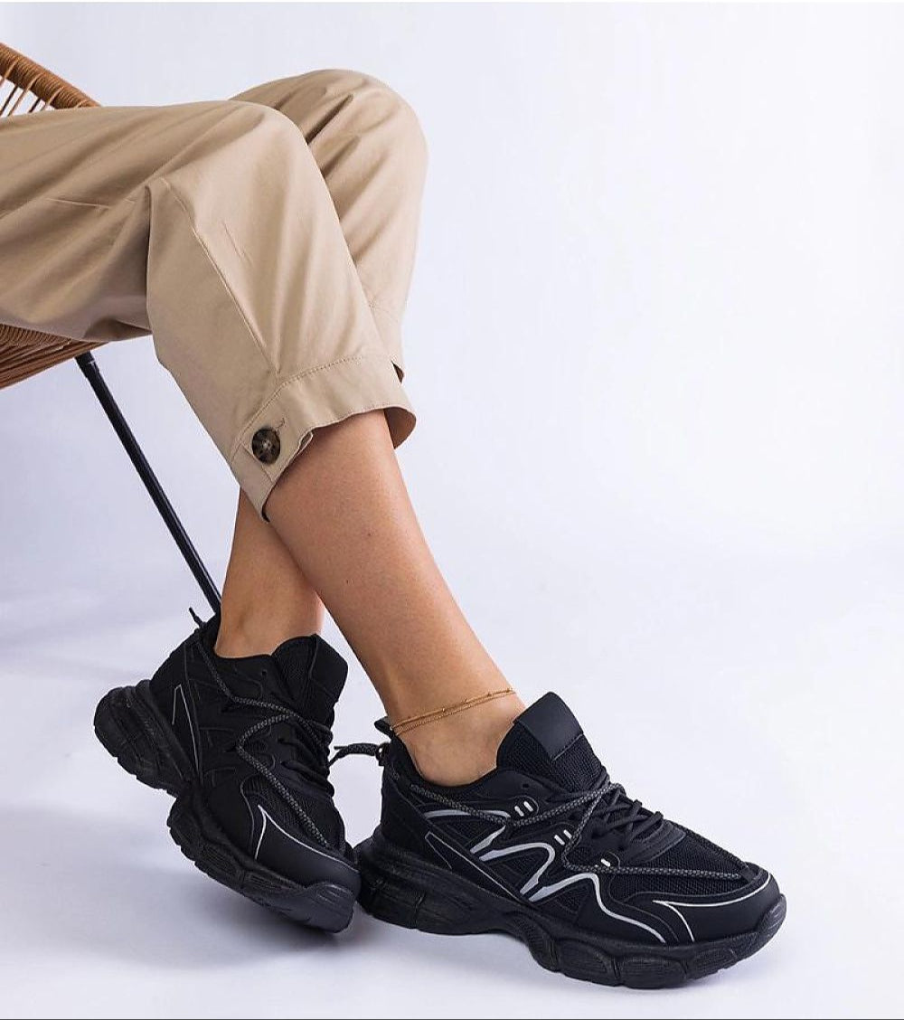 Person wearing black Yndessa Sculpted Sole Lace Sneakers with beige pants, showcasing the sleek design and modern structure.