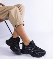 Person wearing black Yndessa Sculpted Sole Lace Sneakers with beige pants, showcasing the sleek design and modern structure.