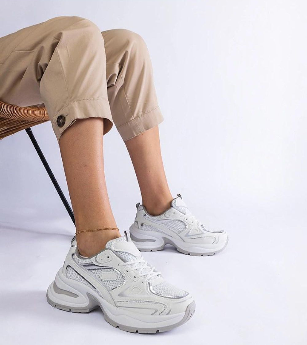 Elphira White Chunky Sole Sneakers with eco leather upper and gray rubber platform, worn by a seated person in beige pants.