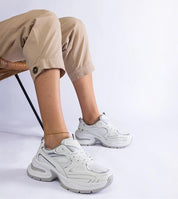 Elphira White Chunky Sole Sneakers with eco leather upper and gray rubber platform, worn by a seated person in beige pants.