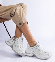 Elphira White Chunky Sole Sneakers with eco leather upper and gray rubber platform, worn with beige pants for a contemporary look.