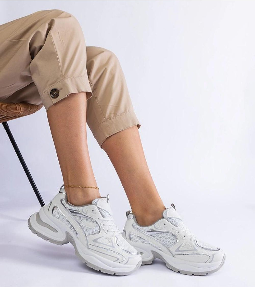 Person wearing Elphira White Chunky Sole Sneakers with eco leather upper and gray rubber sole, sitting on a chair.