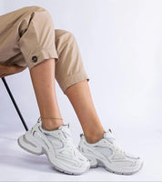 Person wearing Elphira White Chunky Sole Sneakers with eco leather upper and gray rubber sole, sitting on a chair.