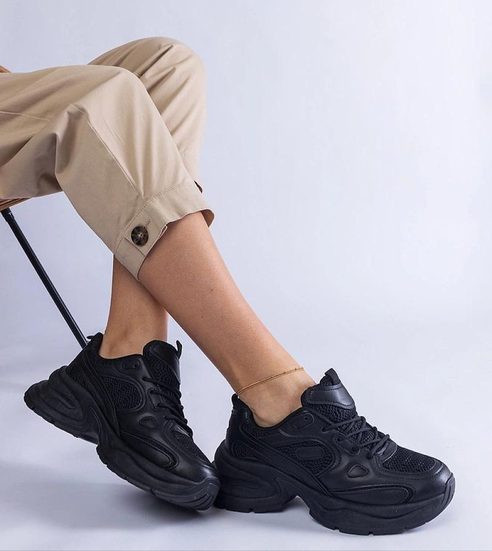 Person wearing black chunky sneakers sitting on a chair, highlighting modern style and comfort with a minimalist aesthetic.