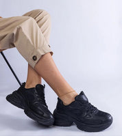 Person wearing black chunky sneakers sitting on a chair, highlighting modern style and comfort with a minimalist aesthetic.