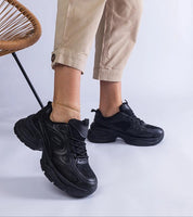 Black chunky sole sneakers with lace-up design, paired with beige pants, showcasing a trendy and modern footwear style.