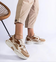 Person wearing camel and white sneakers with chunky sole, paired with beige pants, showcasing a casual look.