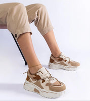 Person wearing Thalvyn Crystal-Tied Brown Sneakers with eco leather and crystal accents, sitting on chair with light beige trousers.
