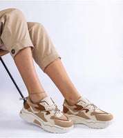 Woman wearing beige camouflage sneakers with white soles, paired with rolled-up khaki pants, sitting on a chair.