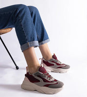 Person wearing Cordevia burgundy-grey urban sneakers with elevated sole and rolled-up jeans, sitting on a chair.