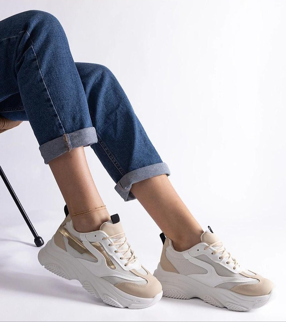 Model wearing beige and white chunky sneakers with cuffed jeans, showcasing a casual chic style against a plain background.