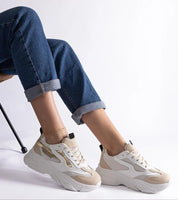Model wearing beige and white chunky sneakers with cuffed jeans, showcasing a casual chic style against a plain background.
