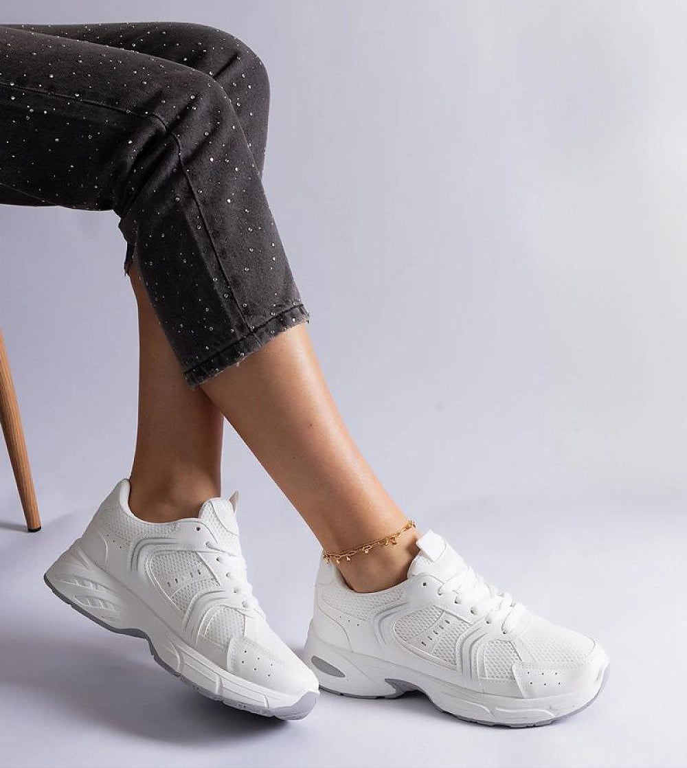 Woman wearing Melvyna White Motion Sneakers with eco leather upper and gray sole, styled with ankle-length pants in a seated pose.