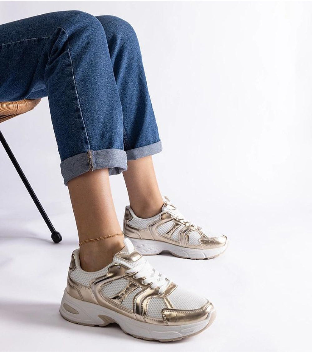 Person wearing white and gold sneakers with blue jeans, highlighting stylish footwear choice and casual outfit.