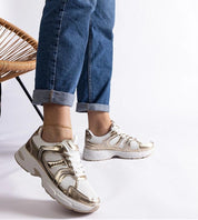 Person wearing gold and white sneakers with jeans, showcasing casual style. Footwear with metallic accents and comfortable design.