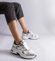 Person wearing Melvyna White Motion Sneakers with eco leather uppers and flexible gray soles, showcasing stylish and sporty footwear.