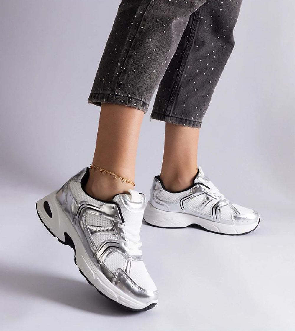 White motion sneakers with flexible gray sole and lace-up design showcased on a person's feet, paired with gray capri pants.