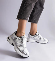 White motion sneakers with flexible gray sole and lace-up design showcased on a person's feet, paired with gray capri pants.
