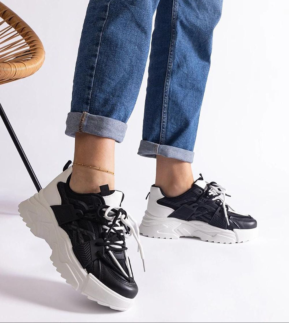 Person wearing black and white urban sneakers with chunky rubber sole, paired with rolled-up jeans.