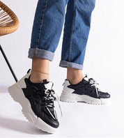 Person wearing black and white urban sneakers with chunky rubber sole, paired with rolled-up jeans.