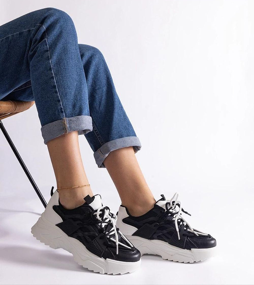 Person wearing black and white chunky sneakers paired with rolled-up jeans sitting on a chair.