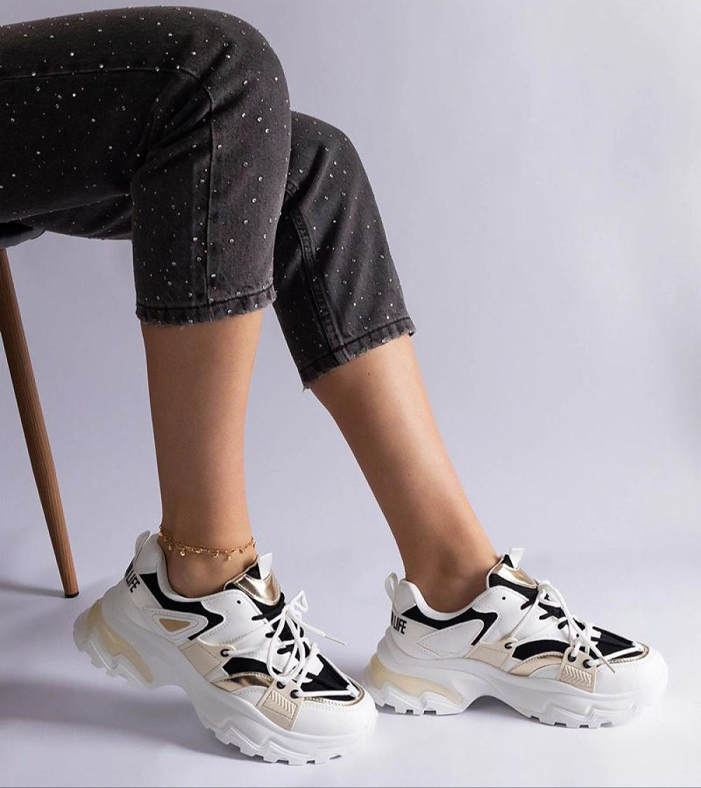 Person wearing Selvyna Contrast Sport Sneakers with eco leather and 5 cm sole in black-and-white, sitting on a chair.