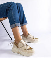 Person wearing stylish chunky beige sneakers with gold accents and blue jeans in a seated position.