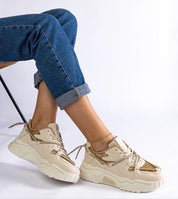 Beige sneakers with gold detailing worn by a seated person in rolled-up jeans.