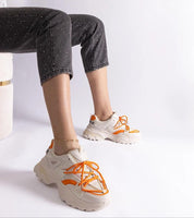Orange and white sporty sneakers worn with black speckled pants, showcasing trendy streetwear style.