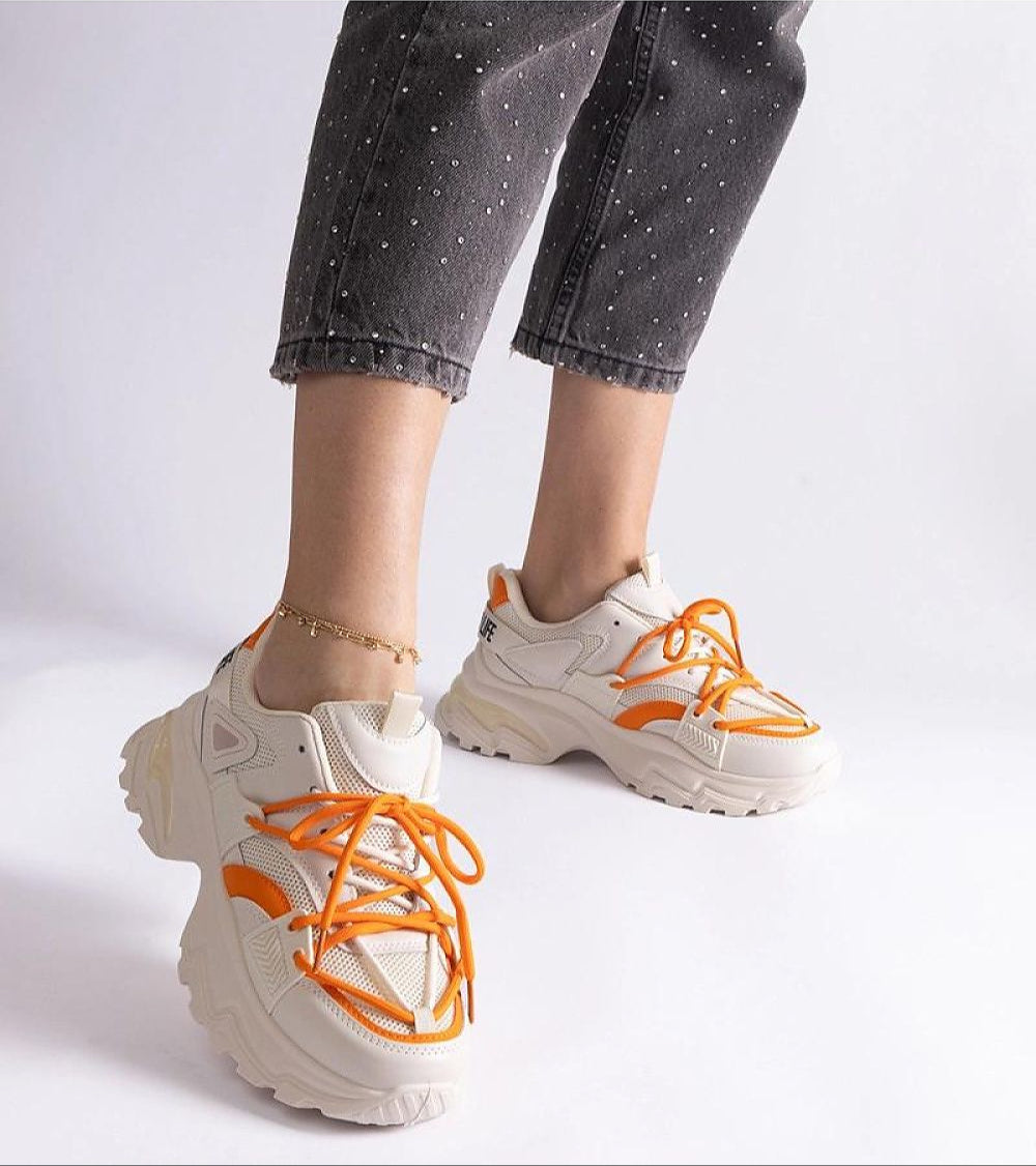 Person wearing stylish chunky sneakers with orange accents and speckled pants, showcasing a trendy and sporty look.