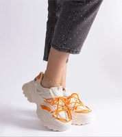 Person wearing white and orange sneakers with lace-up design and thick sole, paired with gray speckled pants.